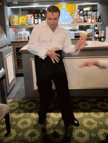 a man in a white shirt and black pants is dancing in a bar
