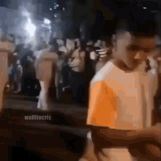 a man in an orange shirt is walking in front of a crowd of people .
