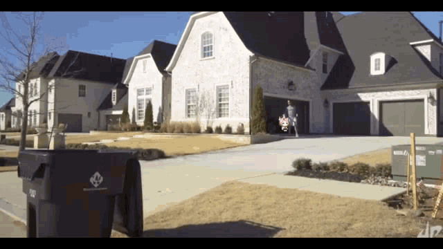 a black trash can with a diamond logo sits in front of a large house