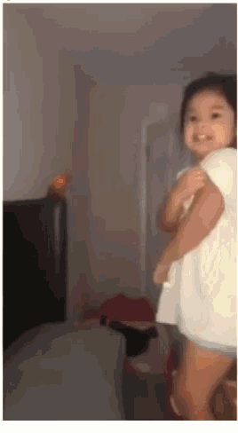 a little girl in a white shirt is standing in a room and smiling