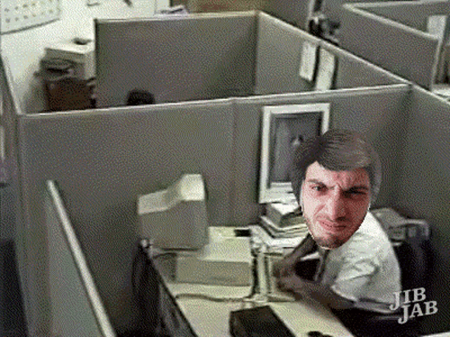 a man sits at a desk in an office cubicle with jib jab written on the cubicle wall