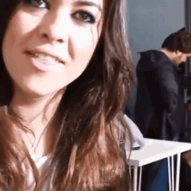 a woman with long hair is smiling and looking at the camera while a man stands behind her .
