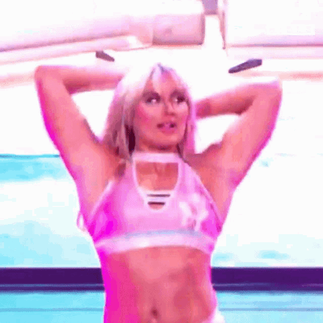 a woman in a pink crop top is standing on a stage with her arms behind her head .