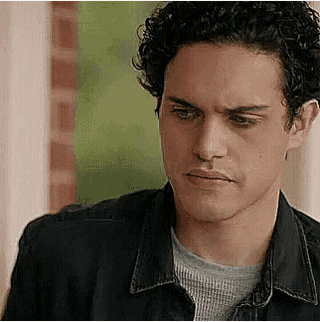 a close up of a man 's face with curly hair wearing a black jacket and a grey shirt .