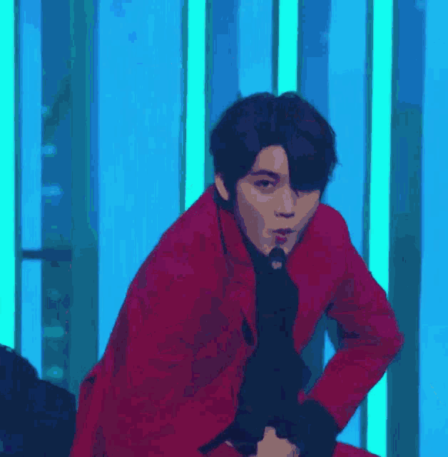 a man in a red suit is singing into a microphone while sitting on a stage .