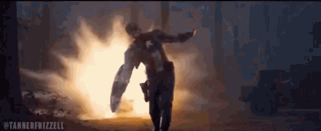 captain america is holding his shield in front of a large explosion .