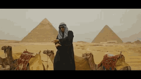 a man in a turban stands in front of pyramids and camels