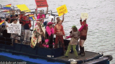 a group of people on a boat holding up signs including one that says allow same sex marriage at sea