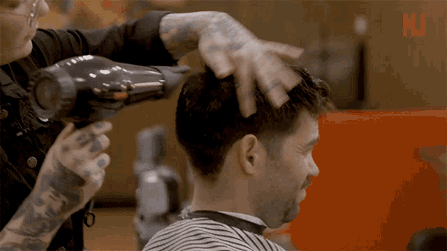 a man is getting his hair blow dried by a barber with a tattooed arm