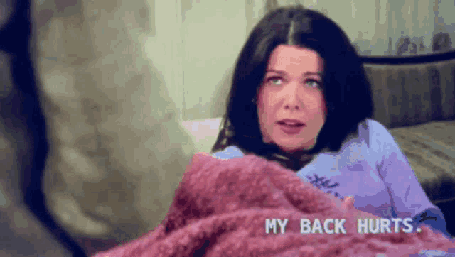 a woman is laying on a bed with a blanket and the words " my back hurts " above her