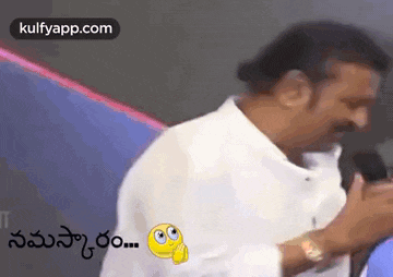a man in a white shirt is talking into a microphone with a smiley face on it .