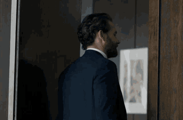 a man in a suit is standing in a doorway looking at a picture on a wall .