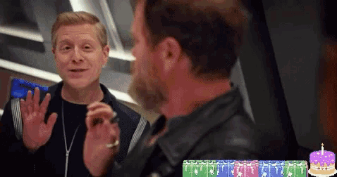 two men are standing next to each other with a birthday cake in the background .