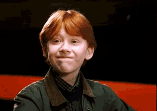 a young boy with red hair is wearing a green jacket and making a funny face