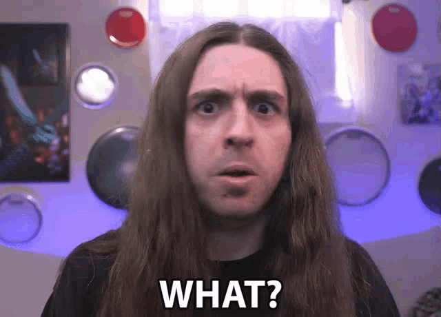 a man with long hair says " what " in front of drums