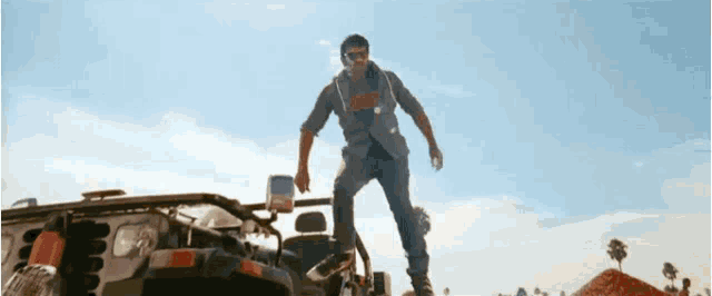 a man is standing on the hood of a vehicle .