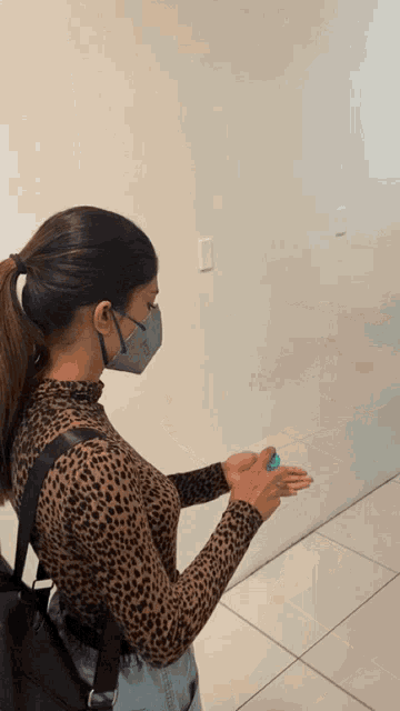 a woman wearing a mask and a leopard print top is washing her hands