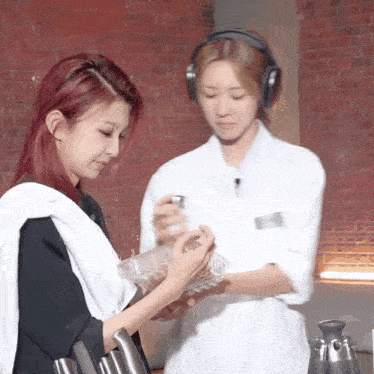 two women standing next to each other one wearing headphones and the other holding a bottle