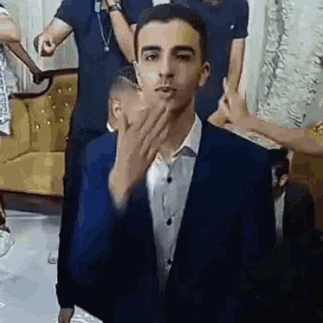 a man in a suit is blowing a kiss at the camera while standing in front of a group of people .