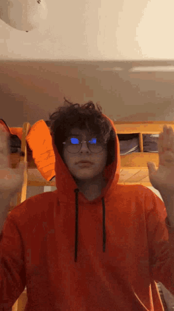 a young man wearing glasses and an orange hoodie is standing in front of a bunk bed