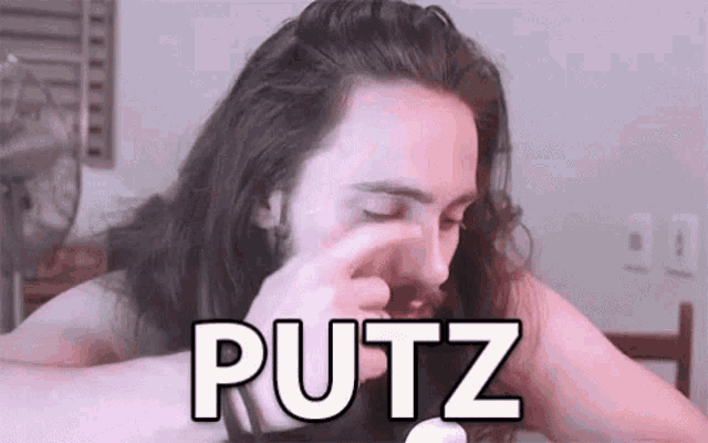a man with long hair and a beard is rubbing his nose with his finger .