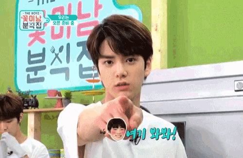 a young man is pointing at the camera while wearing a white shirt with chinese writing on it .