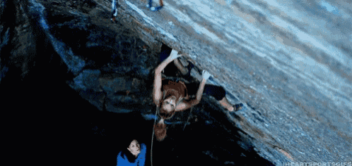a woman is hanging upside down on a rock while another person watches .