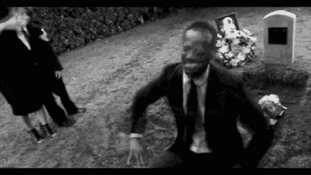 a man in a suit is kneeling down in front of a grave .