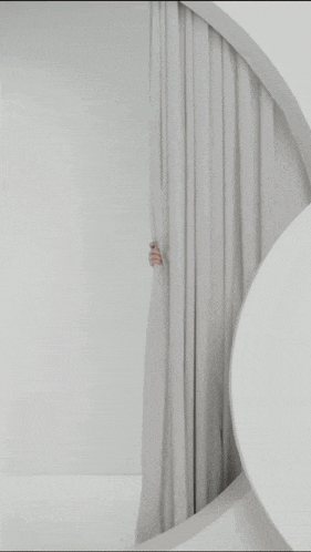 a woman is peeking out from behind a white curtain