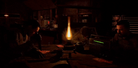 a group of people are sitting around a table with a lamp in the dark .