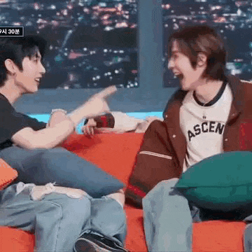 two young men are sitting on a red couch laughing and talking .