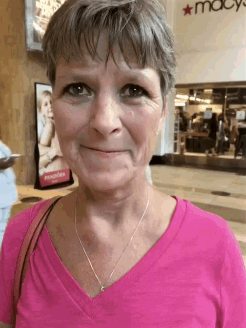 a woman in a pink shirt is smiling in front of a macy 's store