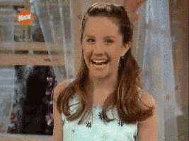 a young girl is laughing in front of a window with a nickelodeon logo on it .