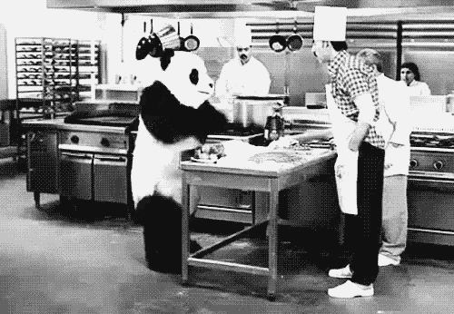 a panda bear is standing in a kitchen next to a table .