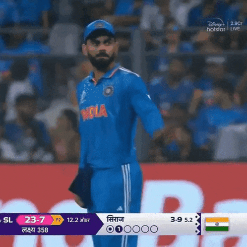 a man in a blue india jersey stands on a soccer field