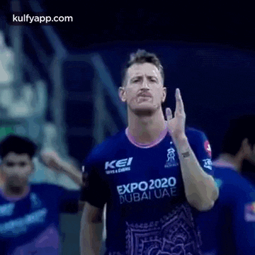 a man in a blue shirt is holding a cricket ball in his hand .