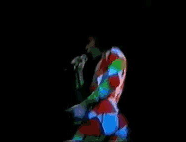 a man in a colorful suit is singing into a microphone in a dark room