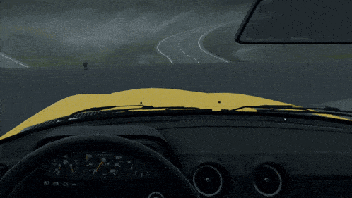 a yellow car is driving down a road with a man standing on the side of the road