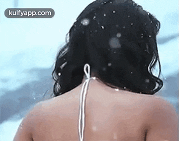 a woman in a white bikini is standing in the snow and looking at the camera .