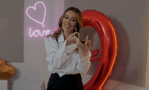 a woman is taking a picture of herself in front of a heart shaped balloon that says love