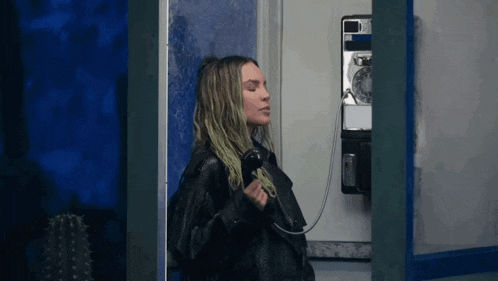 a woman in a black jacket is talking on a payphone