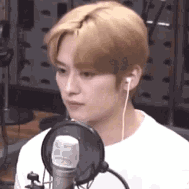 a young man wearing headphones and a white shirt is standing in front of a microphone .