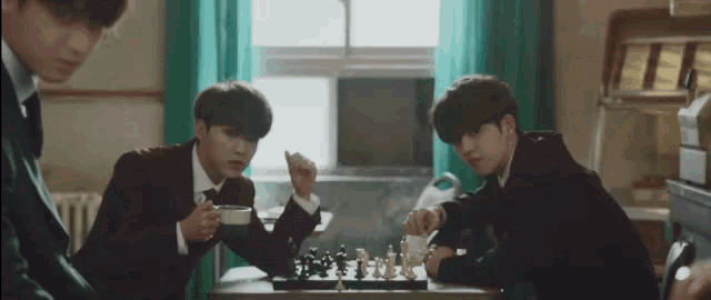 a group of young men are sitting at a table playing chess and drinking coffee .