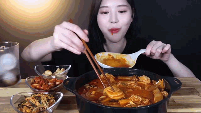 a woman is eating a stew with chopsticks and a ladle