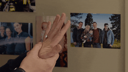a man holds a woman 's hand with a ring on it in front of a picture of a family