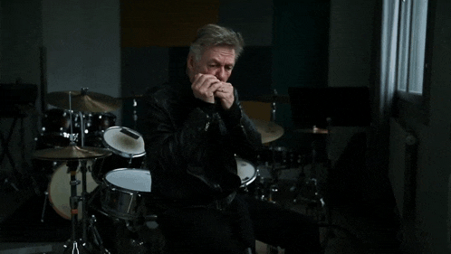 a man playing a harmonica while sitting in front of a drum set