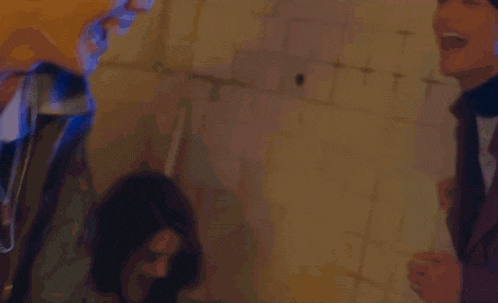 a man is pointing a gun at another man while they are standing next to each other in a dark room .