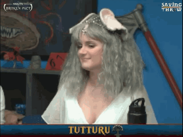 a woman in a white dress is sitting in front of a screen that says ' tuttiru ' on it