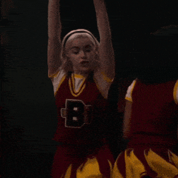 a cheerleader is covering her ears with her hands while another cheerleader is flying in the background .