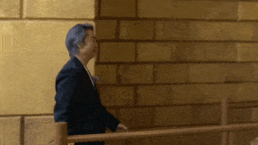 a man in a suit is walking down a staircase in front of a brick wall